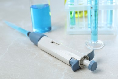 Laboratory analysis. Micropipette and different glassware with liquids on light grey marble table, closeup