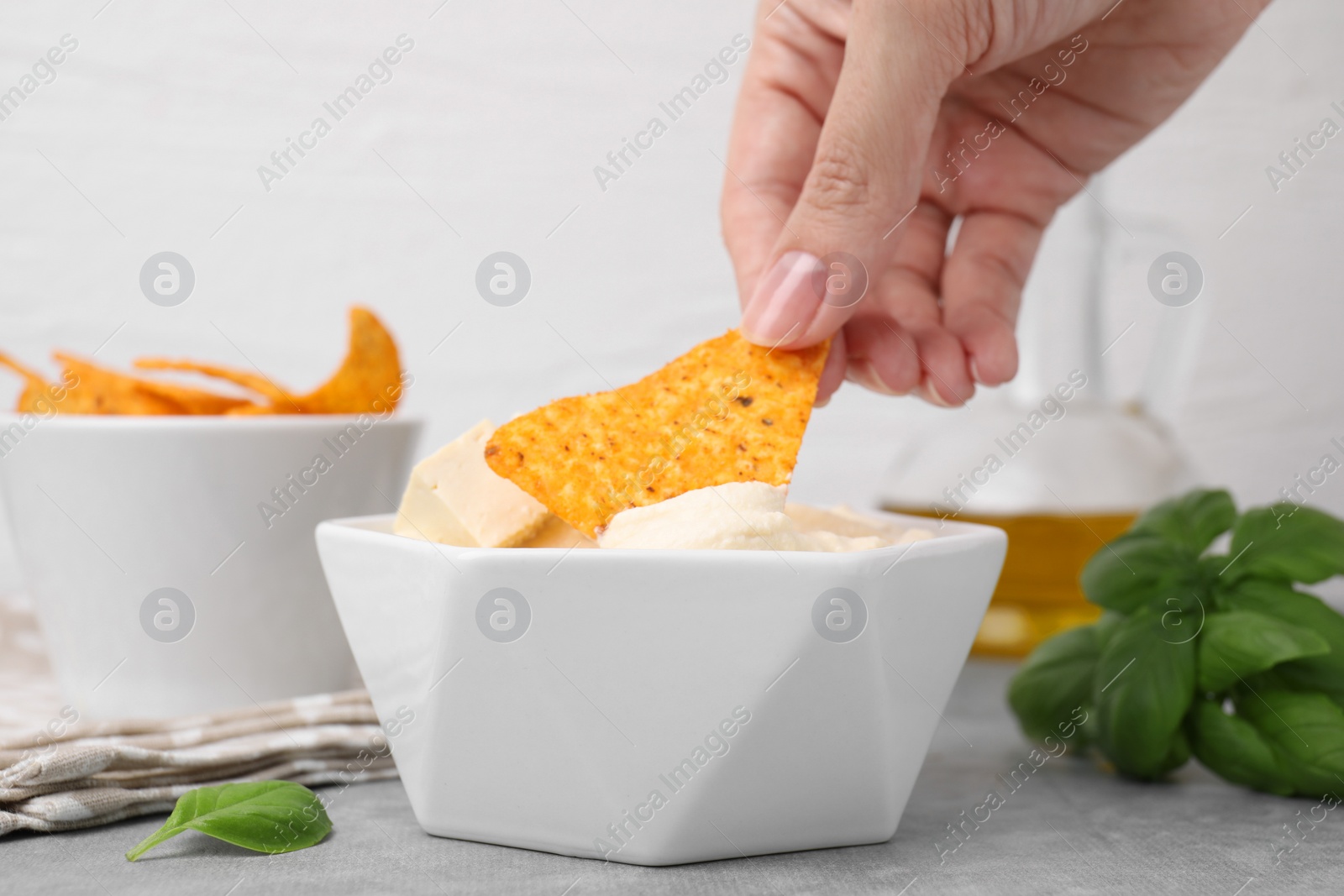 Photo of Woman dipping nachos chip into delicious tofu sauce at grey table, closeup