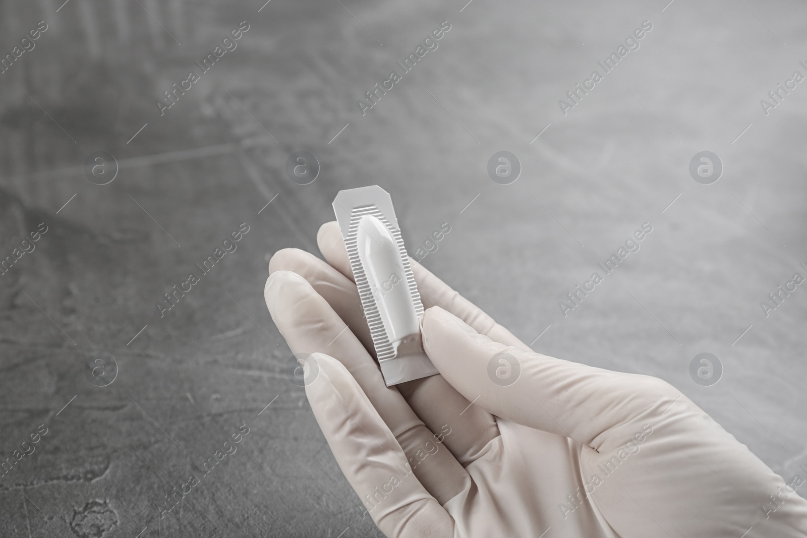 Photo of Woman holding suppository at grey table, closeup. Hemorrhoid treatment