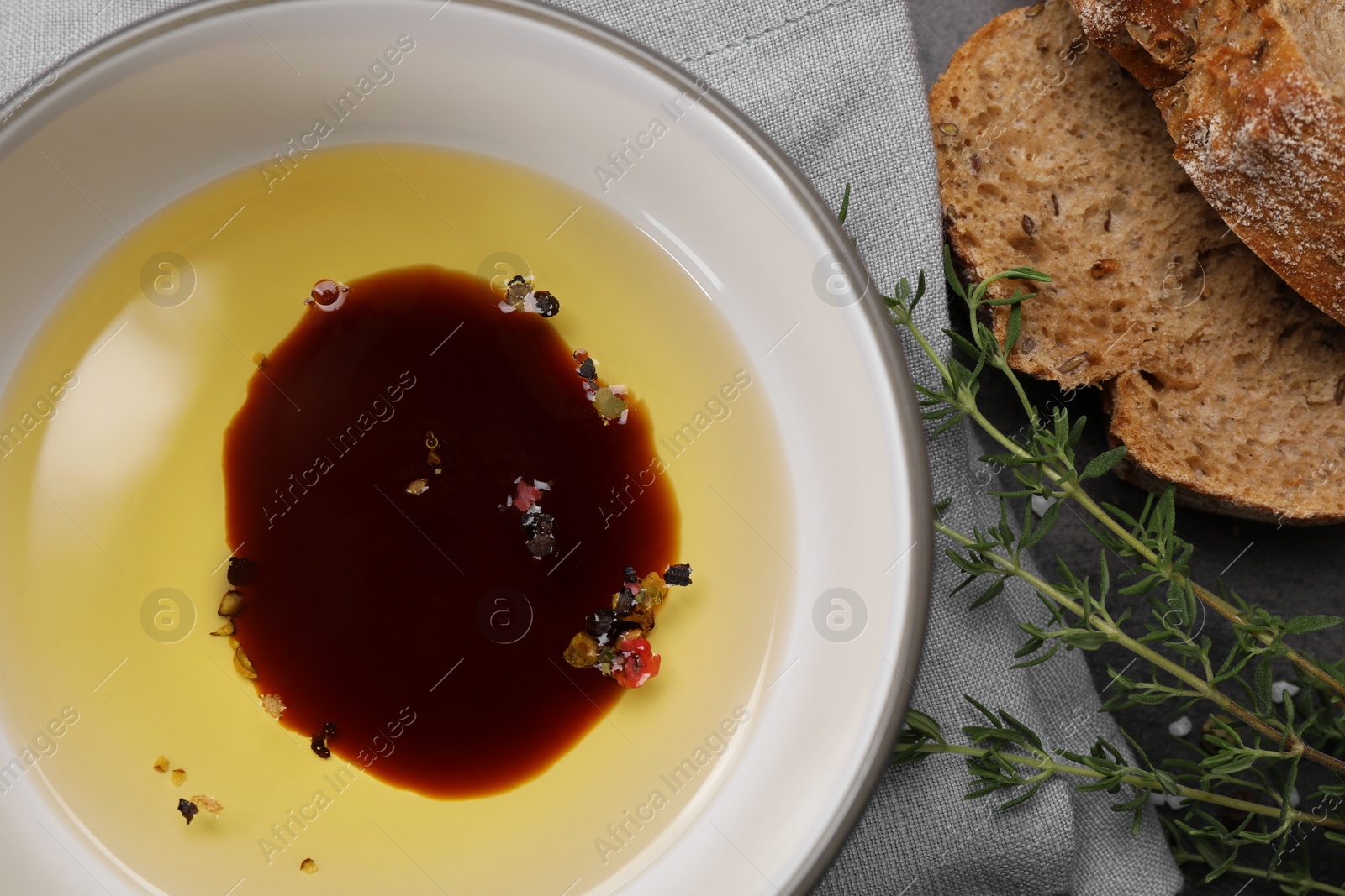 Photo of Bowl of organic balsamic vinegar with oil, spices and bread slices on grey table, flat lay