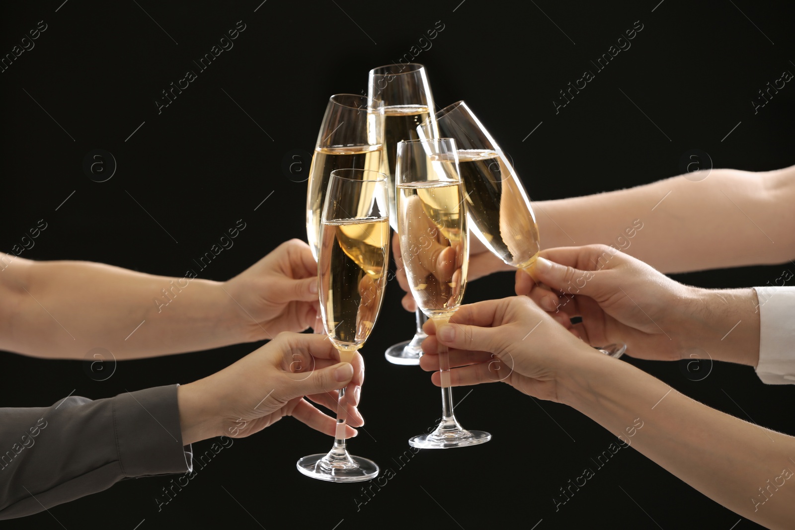 Photo of People clinking glasses of champagne on dark background, closeup