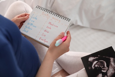 Photo of Pregnant woman with baby names list and sonogram sitting on bed, closeup