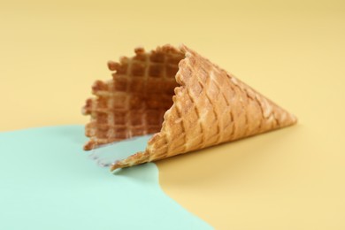 Photo of Melted ice cream and wafer cone on beige background, closeup