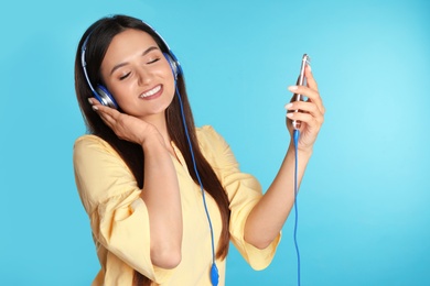 Photo of Attractive woman with mobile phone enjoying music in headphones on color background
