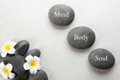 Photo of Stones with words MIND, BODY, SOUL and flowers on light background, flat lay. Zen lifestyle