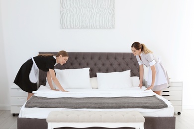 Professional chambermaids making bed in hotel room