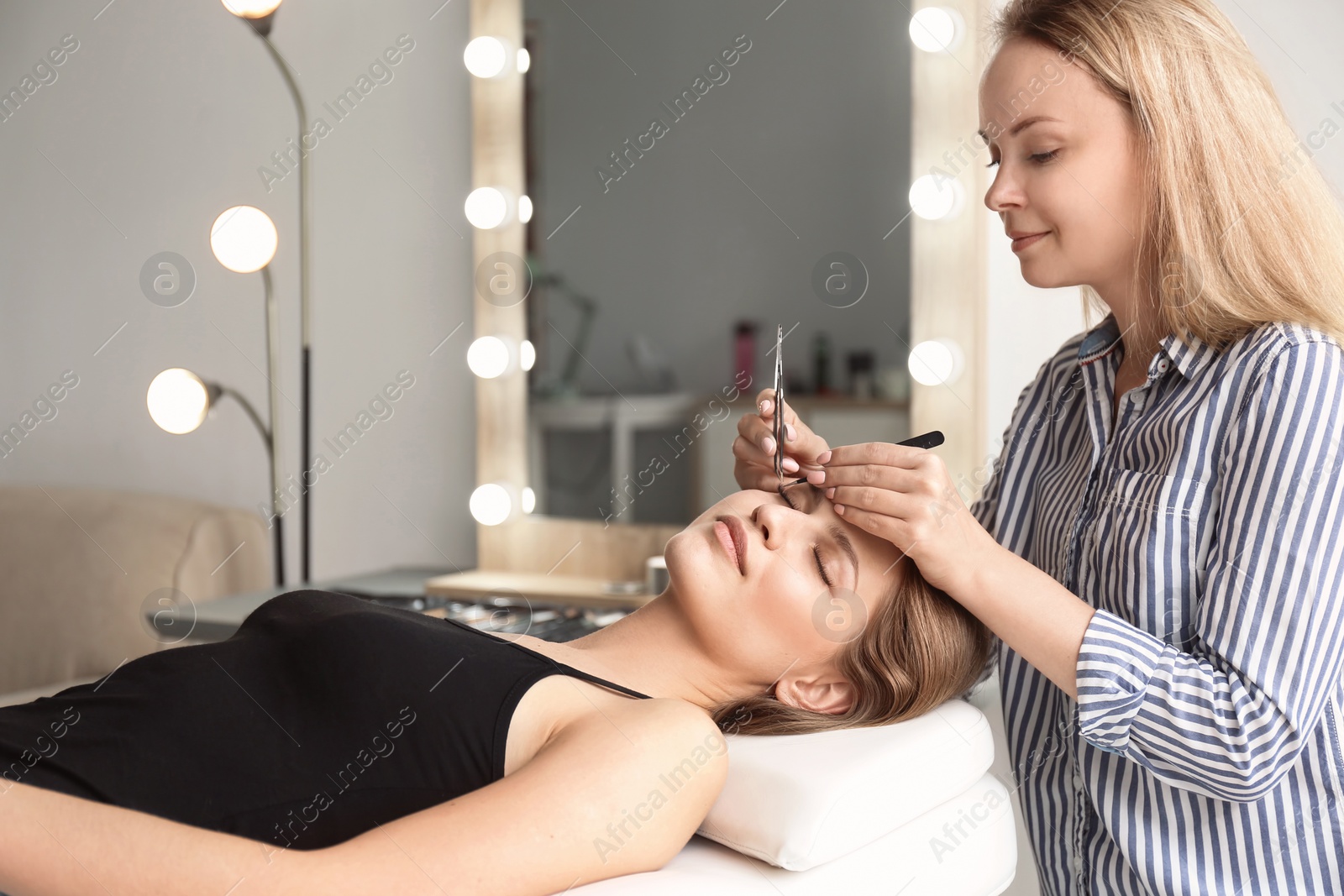 Photo of Young woman undergoing eyelash extensions procedure in salon