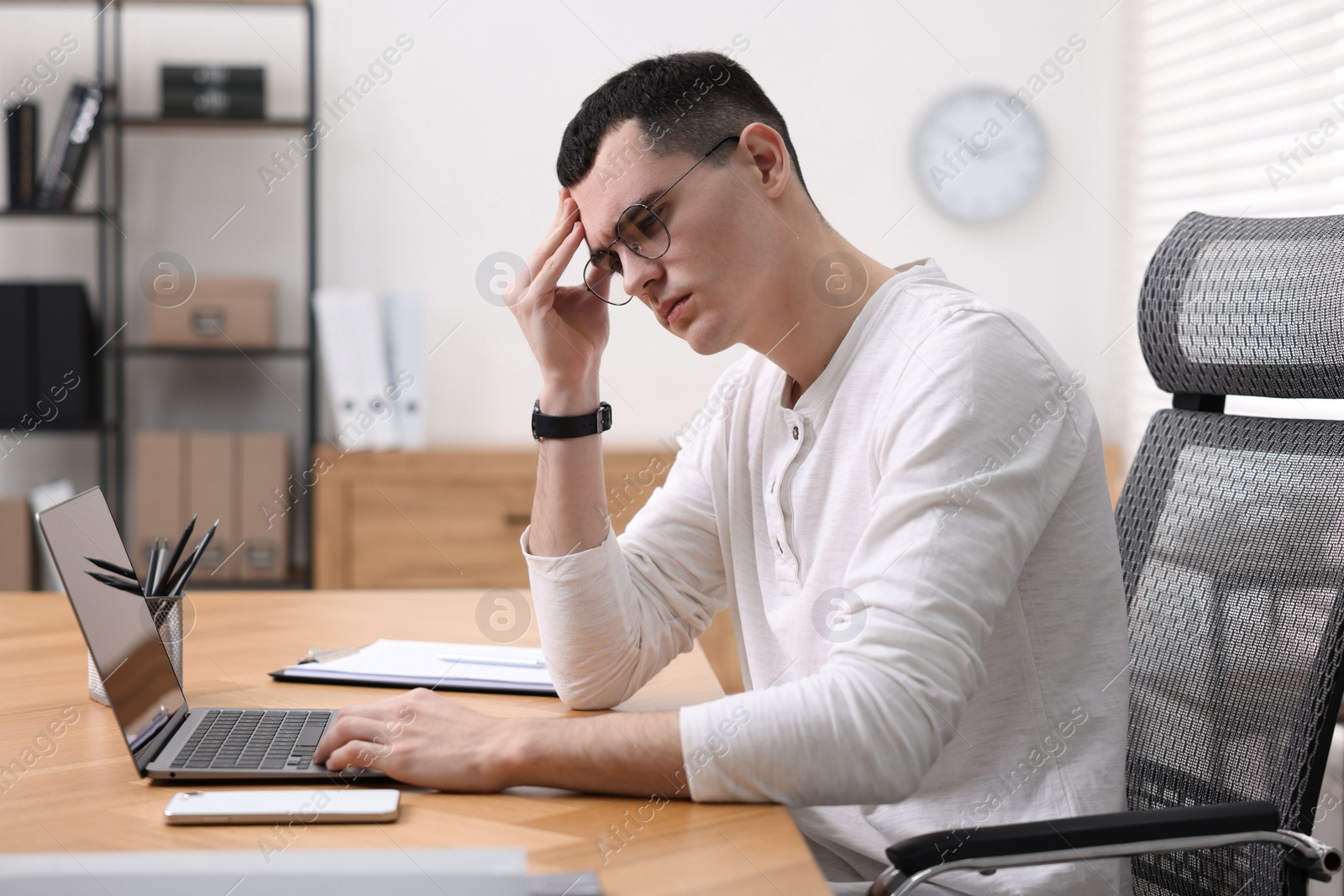 Photo of Young man suffering from headache at workplace in office