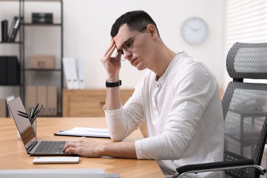 Photo of Young man suffering from headache at workplace in office