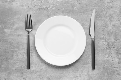 Photo of Clean plate and shiny silver cutlery on light grey table, flat lay