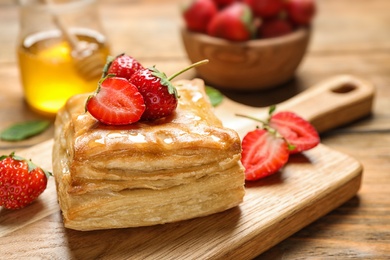 Photo of Fresh delicious puff pastry with sweet strawberries on wooden table, closeup