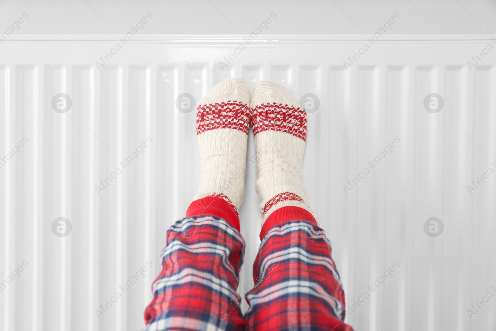 Photo of Little girl warming feet near heating radiator indoors, closeup