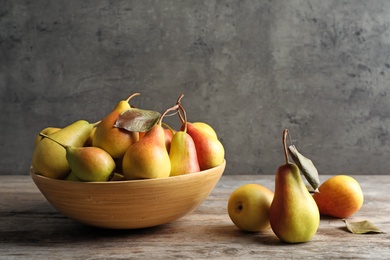 Photo of Bowl with ripe pears on table against grey background