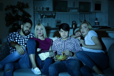 Young friends with snacks watching TV on sofa at night