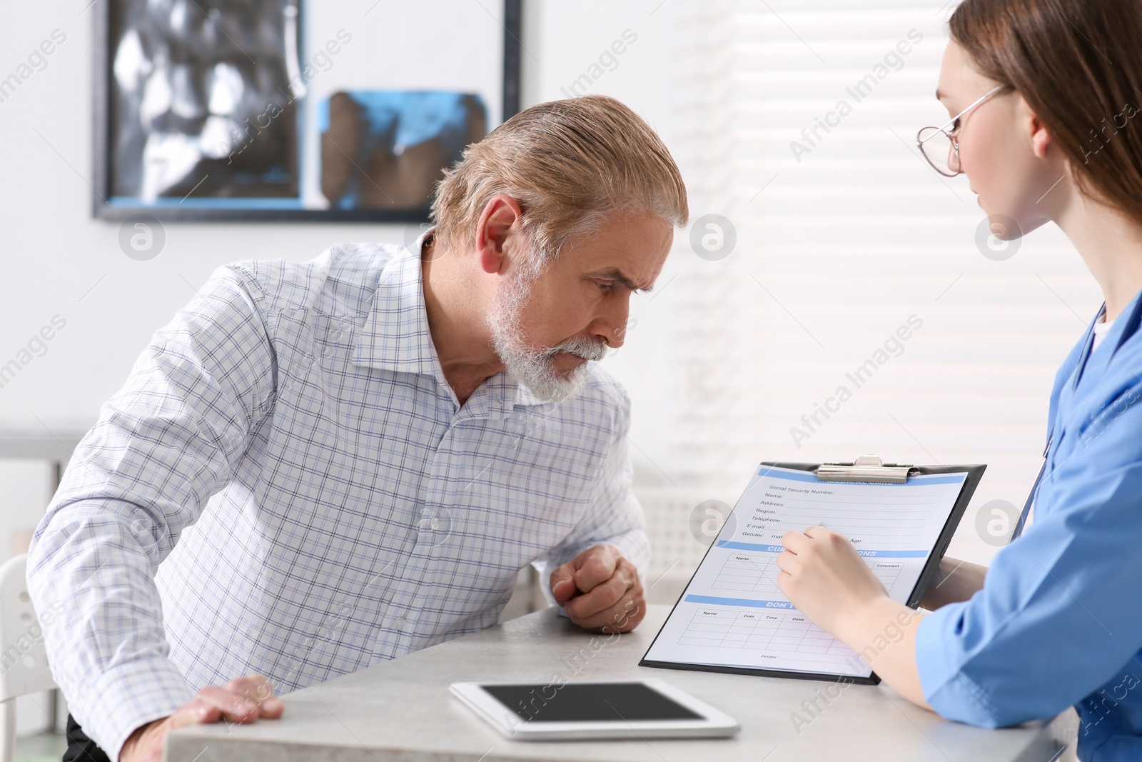 Photo of Doctor showing medical card to patient at table in clinic