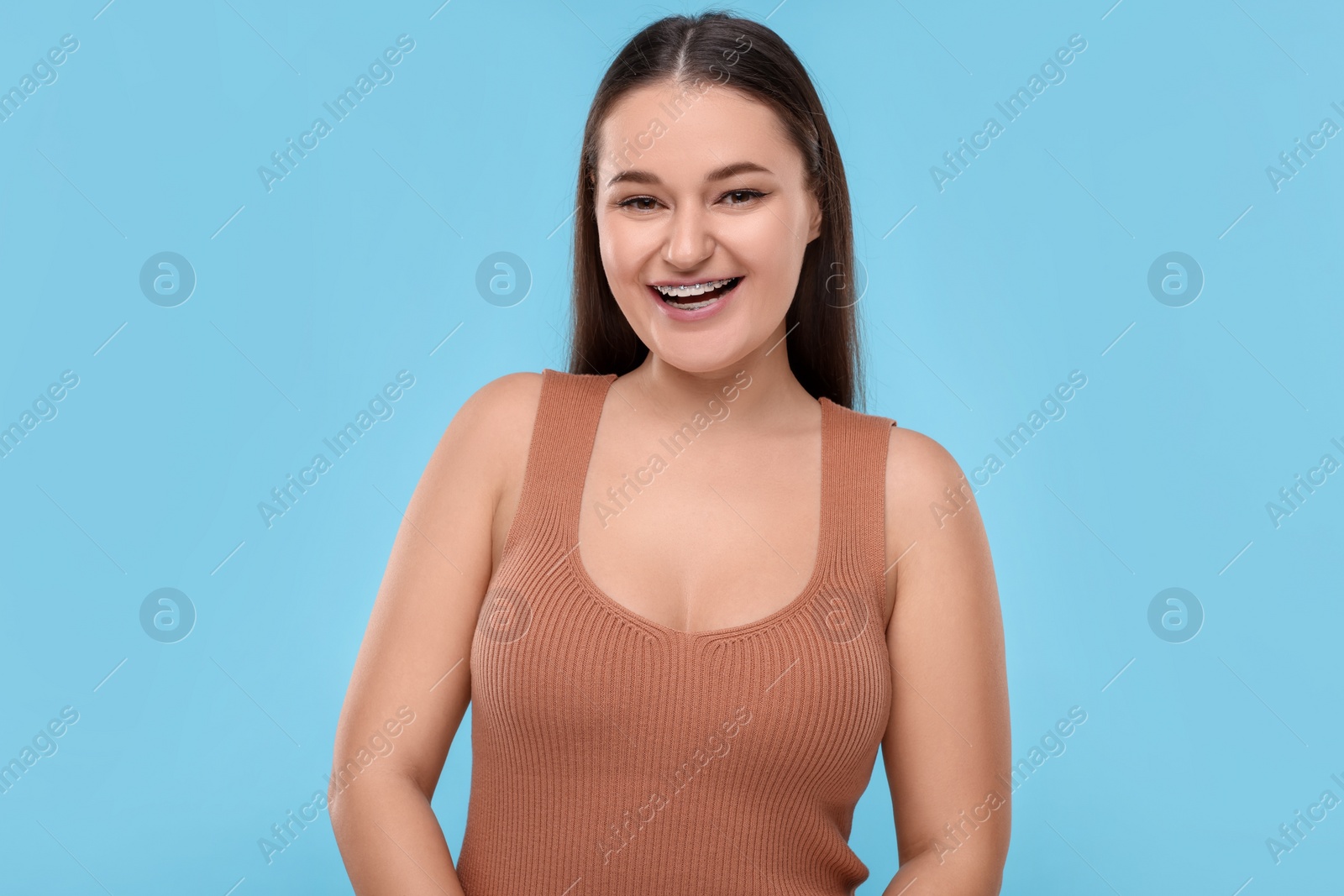 Photo of Happy woman with dental braces on light blue background