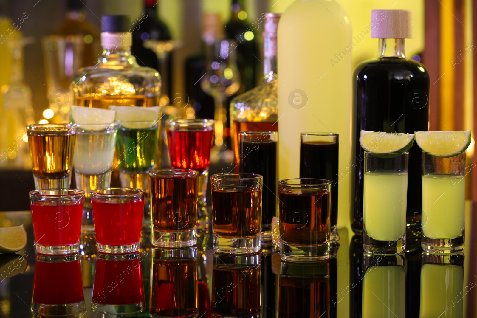 Photo of Different shooters in shot glasses and bottles on mirror surface. Alcohol drink
