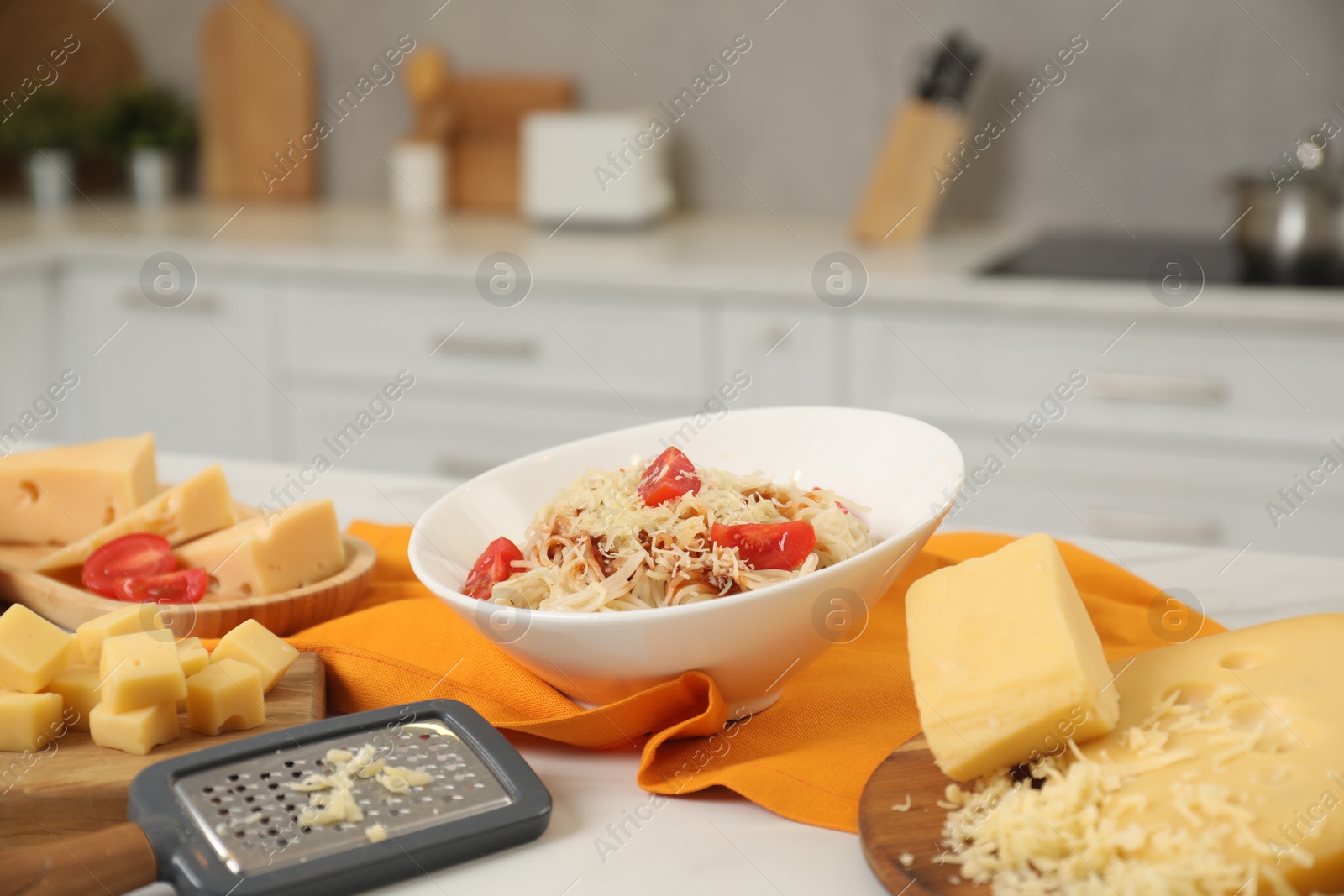 Photo of Delicious pasta with grated cheese and tomatoes on white table in kitchen