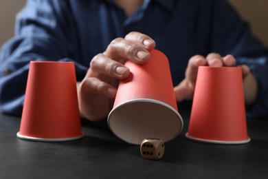 Photo of Woman playing thimblerig game with red cups and dice at black table, closeup