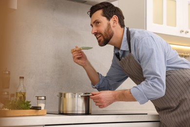Photo of Man tasting delicious soup with spoon in kitchen