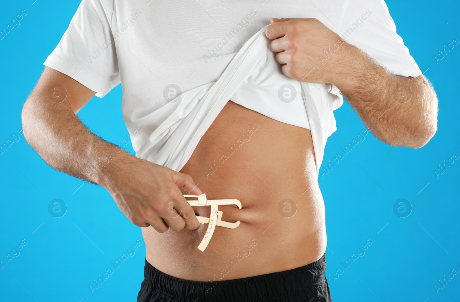 Photo of Man measuring body fat layer with caliper on light blue background, closeup. Nutritionist's tool