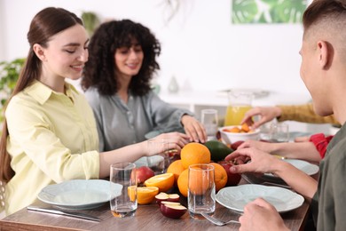 Photo of Vegetarian food. Friends eating fresh fruits at wooden table indoors