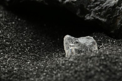 Photo of Shiny rough diamond on decorative black sand. Space for text