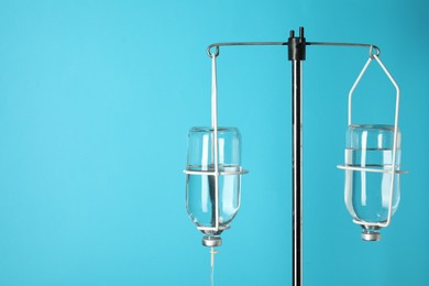 Photo of IV infusion set on pole against light blue background. Space for text