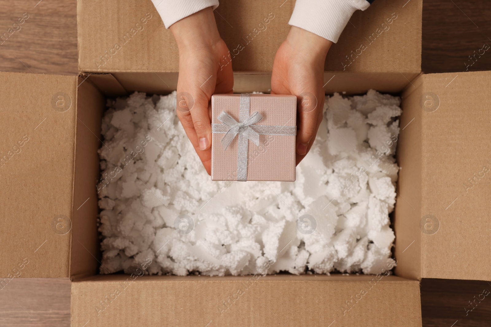 Photo of Woman putting Christmas gift box into parcel at wooden table, top view. Sending present by mail