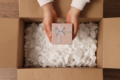 Photo of Woman putting Christmas gift box into parcel at wooden table, top view. Sending present by mail