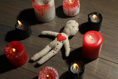 Photo of Voodoo doll with pins in circle of burning candles on wooden table