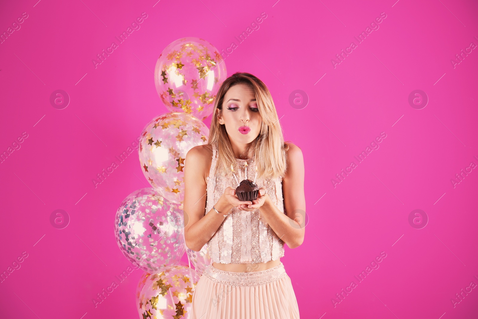 Photo of Young woman with birthday muffin and air balloons on color background