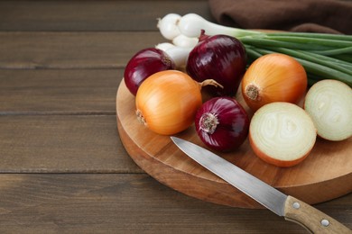 Photo of Board with different kinds of onions on wooden table, closeup. Space for text