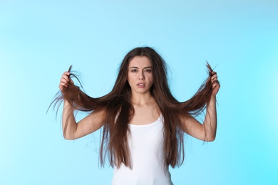 Emotional woman with damaged hair on color background. Split ends