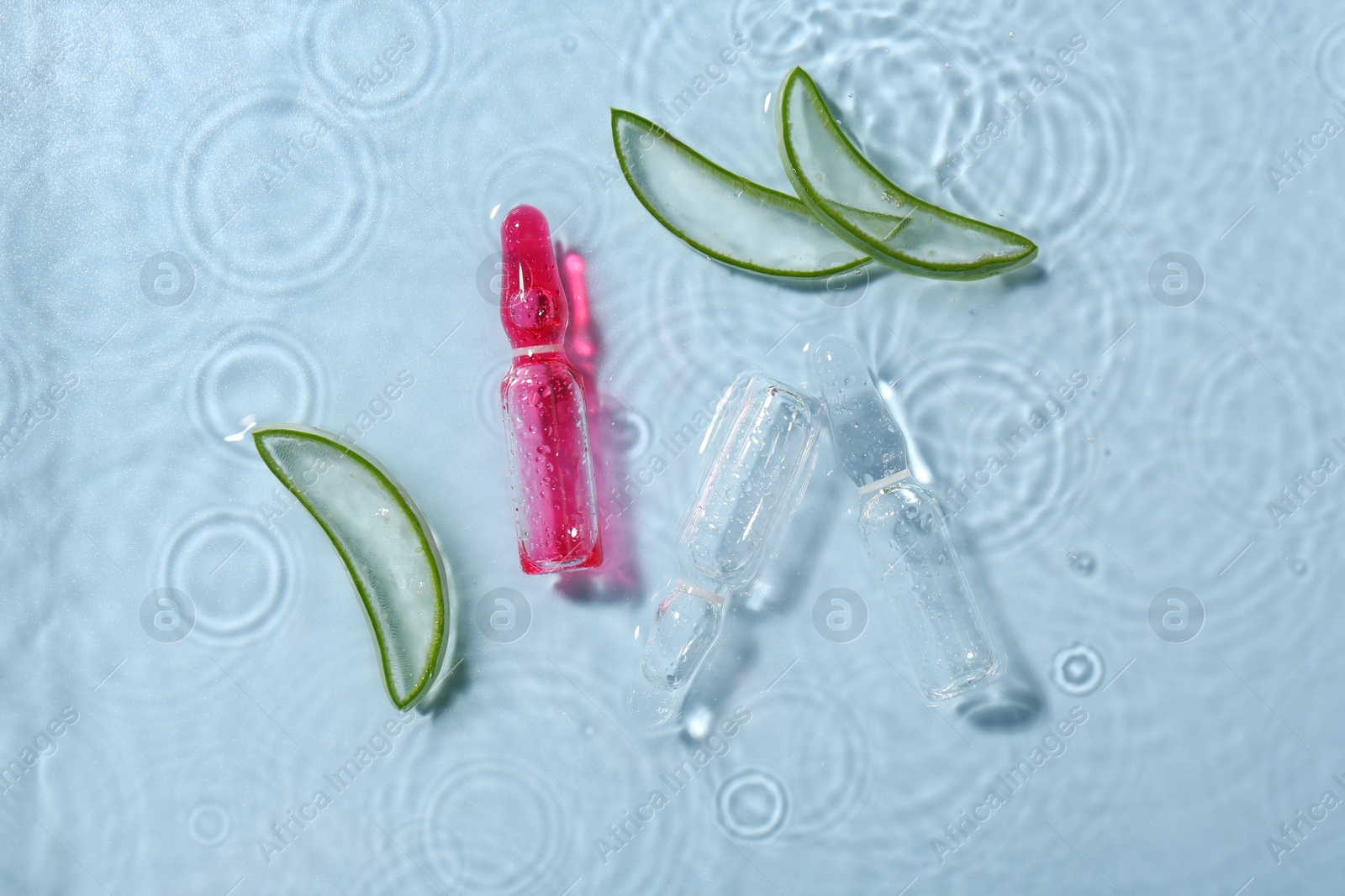 Photo of Skincare ampoules with extract of aloe vera and cut leaves in water on light blue background, flat lay