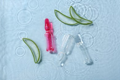 Skincare ampoules with extract of aloe vera and cut leaves in water on light blue background, flat lay