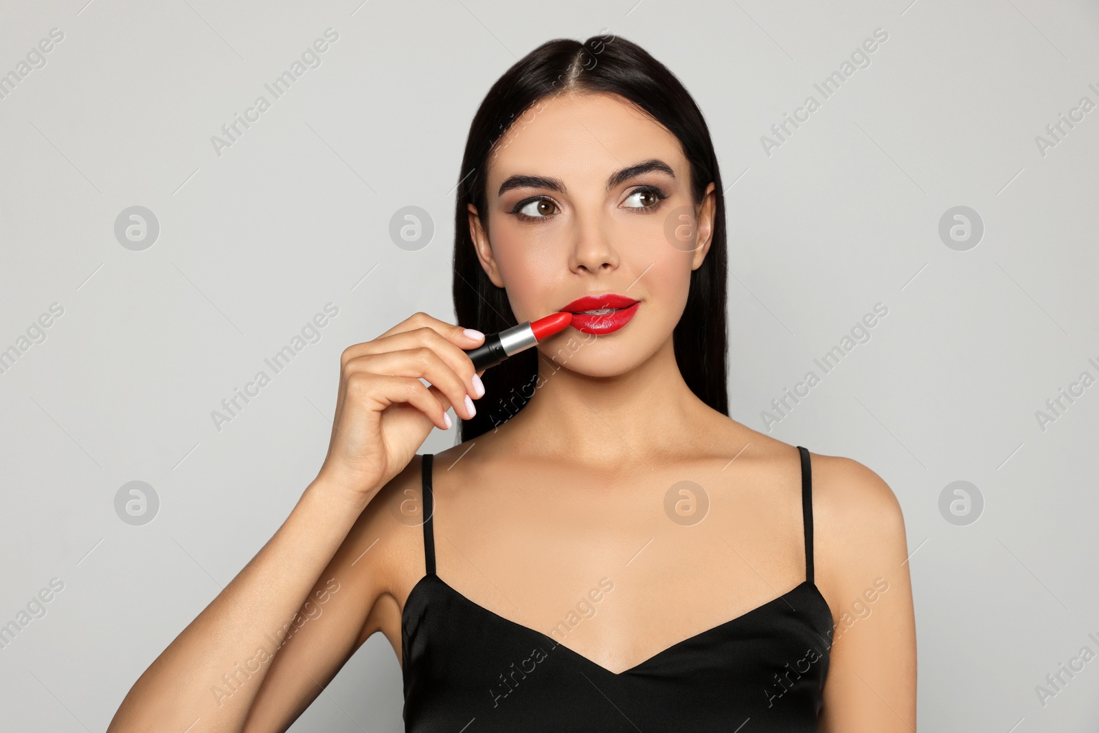 Photo of Young woman applying red lipstick on light gray background