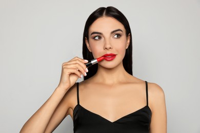 Young woman applying red lipstick on light gray background