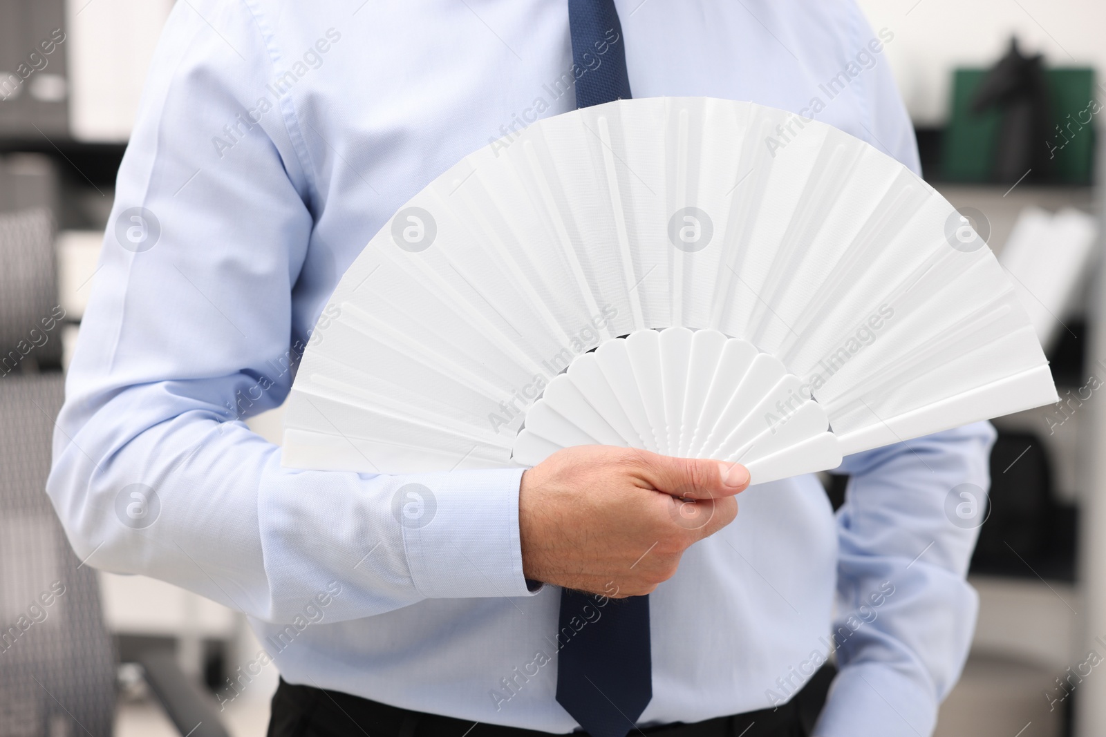 Photo of Businessman with white hand fan in office, closeup