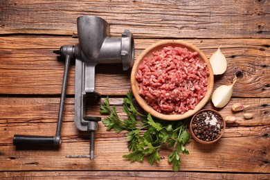 Photo of Manual meat grinder with beef mince, peppercorns, onion and parsley on wooden table, flat lay