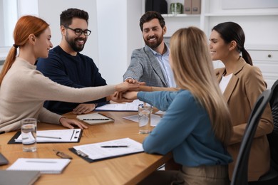 Photo of Team of employees joining hands in office