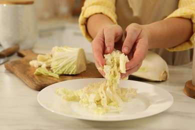 Photo of Woman putting cut Chinese cabbage into plate at white kitchen table, closeup