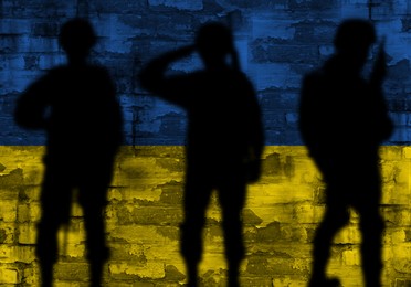 Silhouettes of soldiers and brick wall painted in Ukrainian flag colors on background. Military service during war