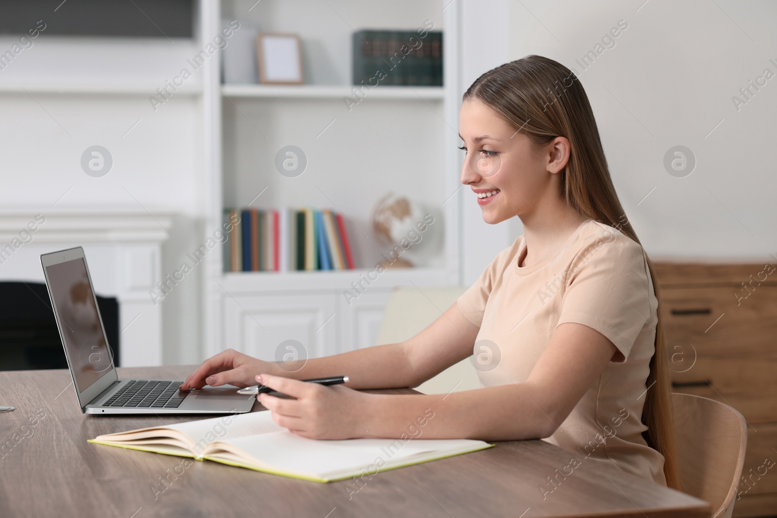 Photo of Online learning. Teenage girl writing in notebook near laptop at home