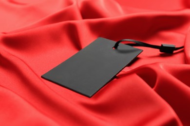 Blank black tag on red silky fabric, closeup. Space for text