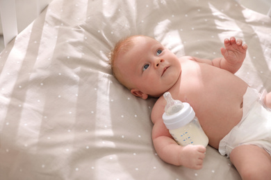 Cute healthy baby with bottle of milk lying in cot