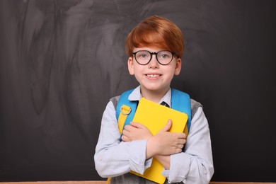 Photo of Portrait of smiling schoolboy with book near blackboard