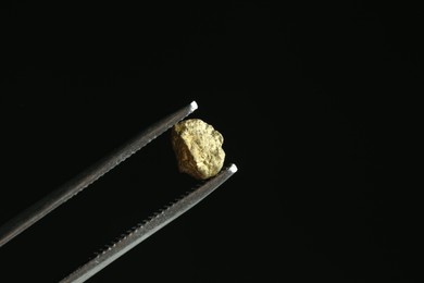 Photo of Tweezers with gold nugget against black background, closeup. Space for text