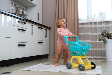 Photo of Cute baby with toy walker in kitchen near window. Learning to walk