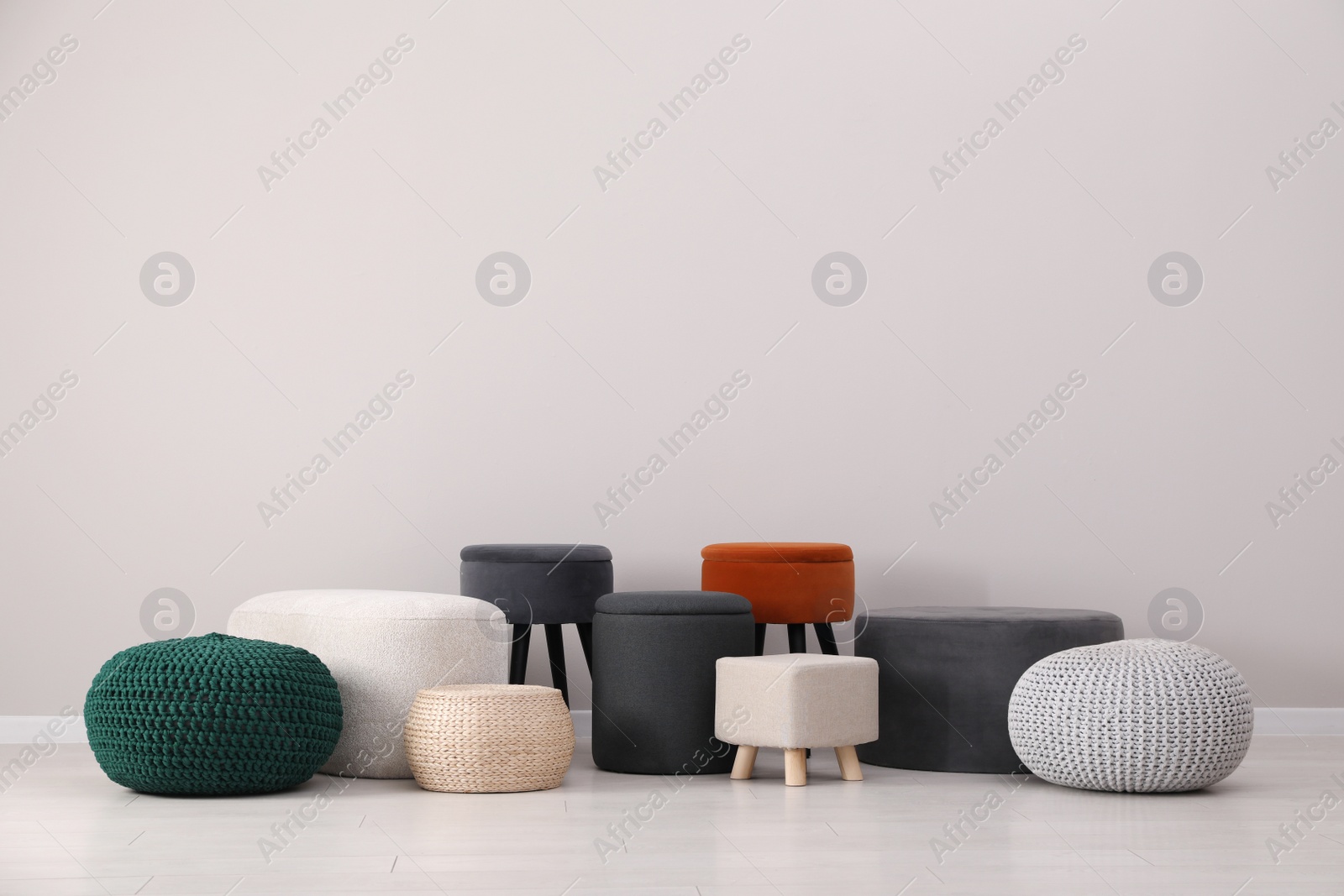 Photo of Different stylish poufs and ottomans near light grey wall